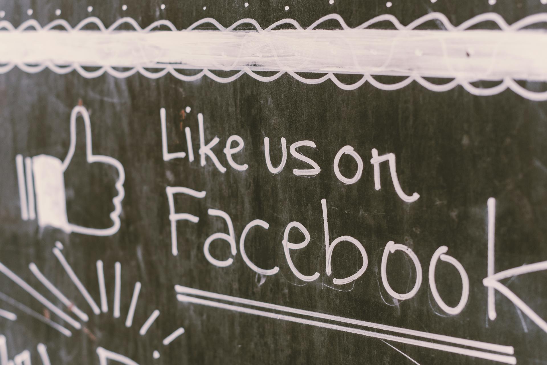 Chalkboard message promotes Facebook engagement.  An unidentifiable business or organization is encouraging customers to "Like us on Facebook."  The message, written in white chalk on a da...