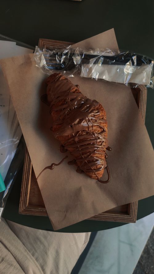 Free Close-up of a croissant drizzled with chocolate on paper, ready to eat. Stock Photo