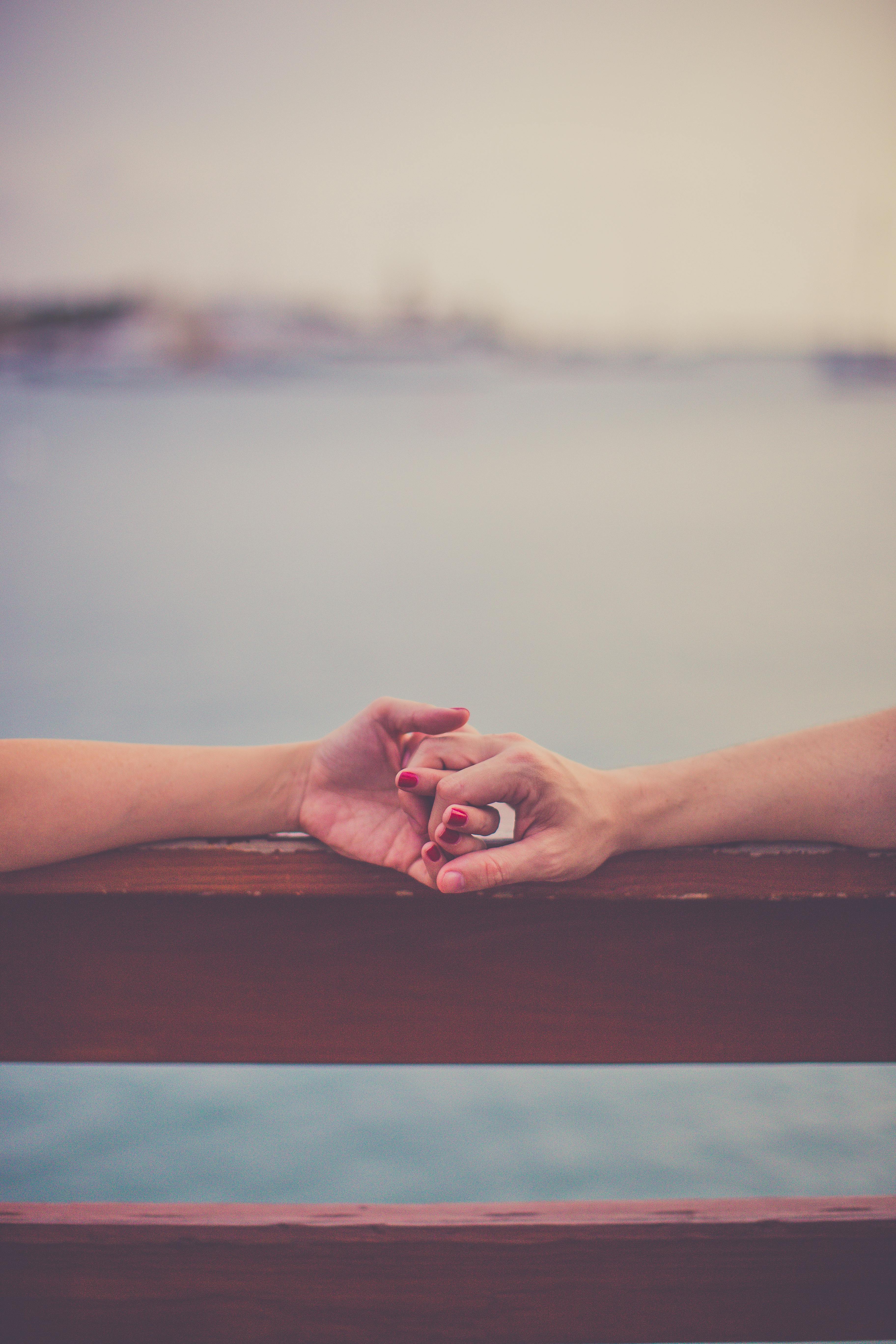 日落时分，两只手轻轻握住水边的木栏杆