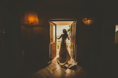 Вид сзади женщины в платье, стоящей на дверном проеме, ведущем на балкон