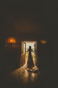 光线昏暗的房间里，一位穿着婚纱的新娘优雅地站在敞开的门口向外张望