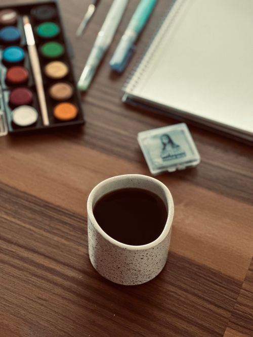 Free Art supplies and a coffee mug create a cozy workspace vibe. Stock Photo