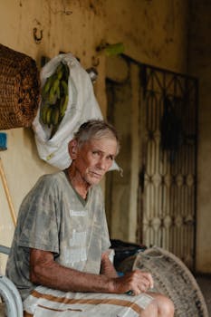 Elderly man sitting outside a rustic home, reflecting rural life.
