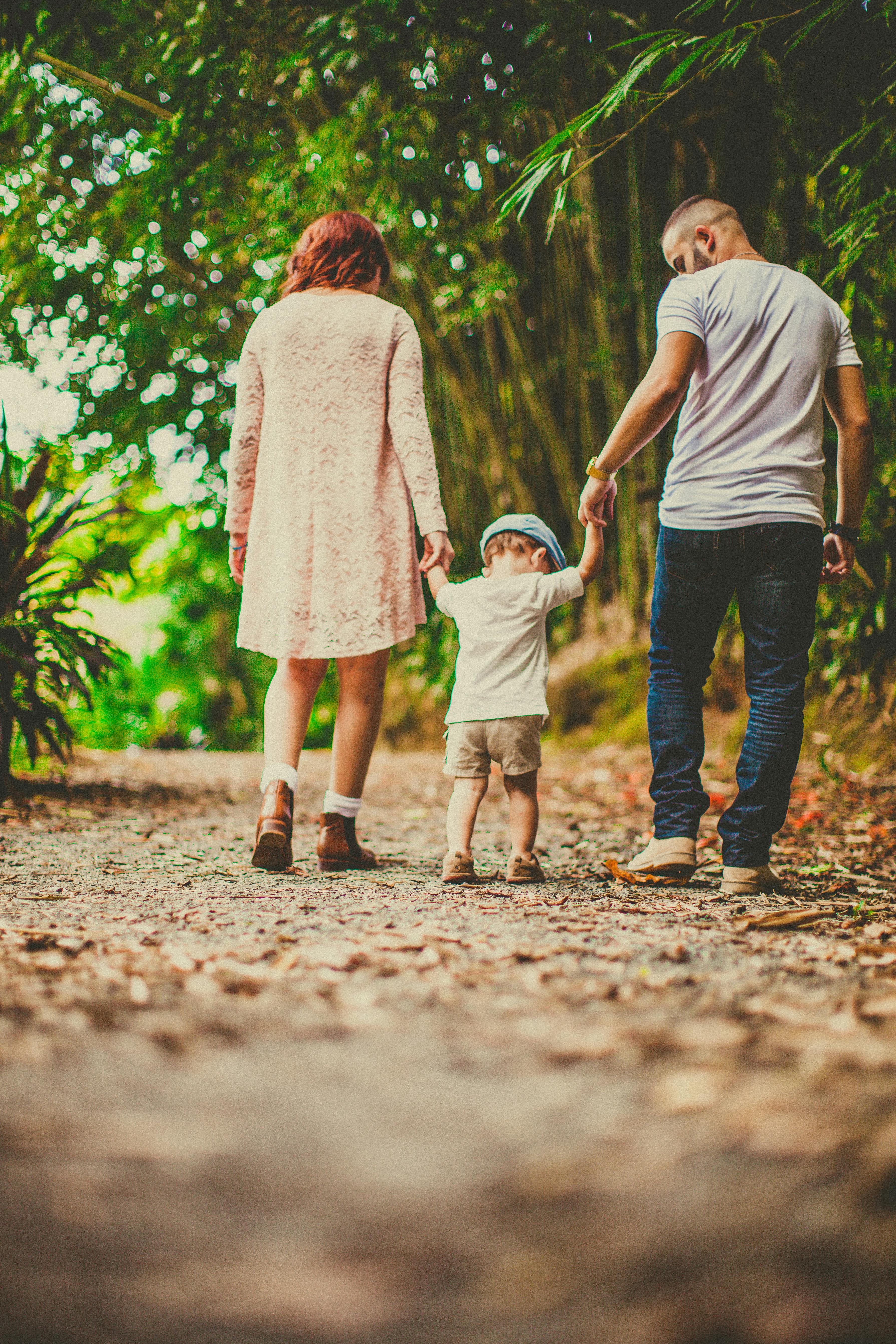 A child held by his parents on each hand while walking outdoors. | Photo: Pexels