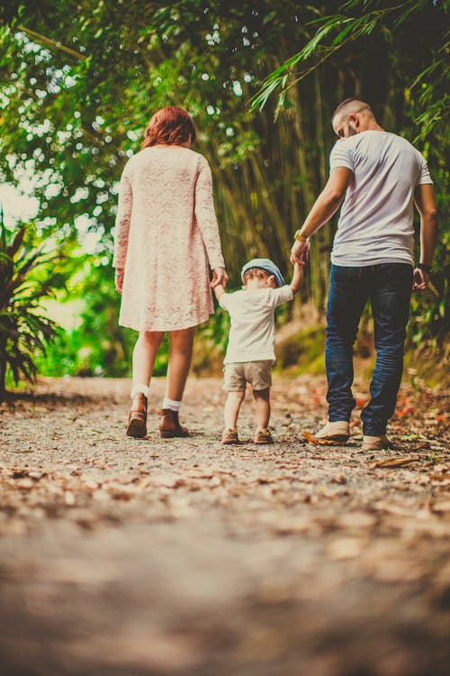 Inquadratura Dal Basso Di Un Bambino Tenuto Da Donna E Uomo Su Ciascuna Mano Che Cammina Su Un Sentiero Sterrato All'aperto