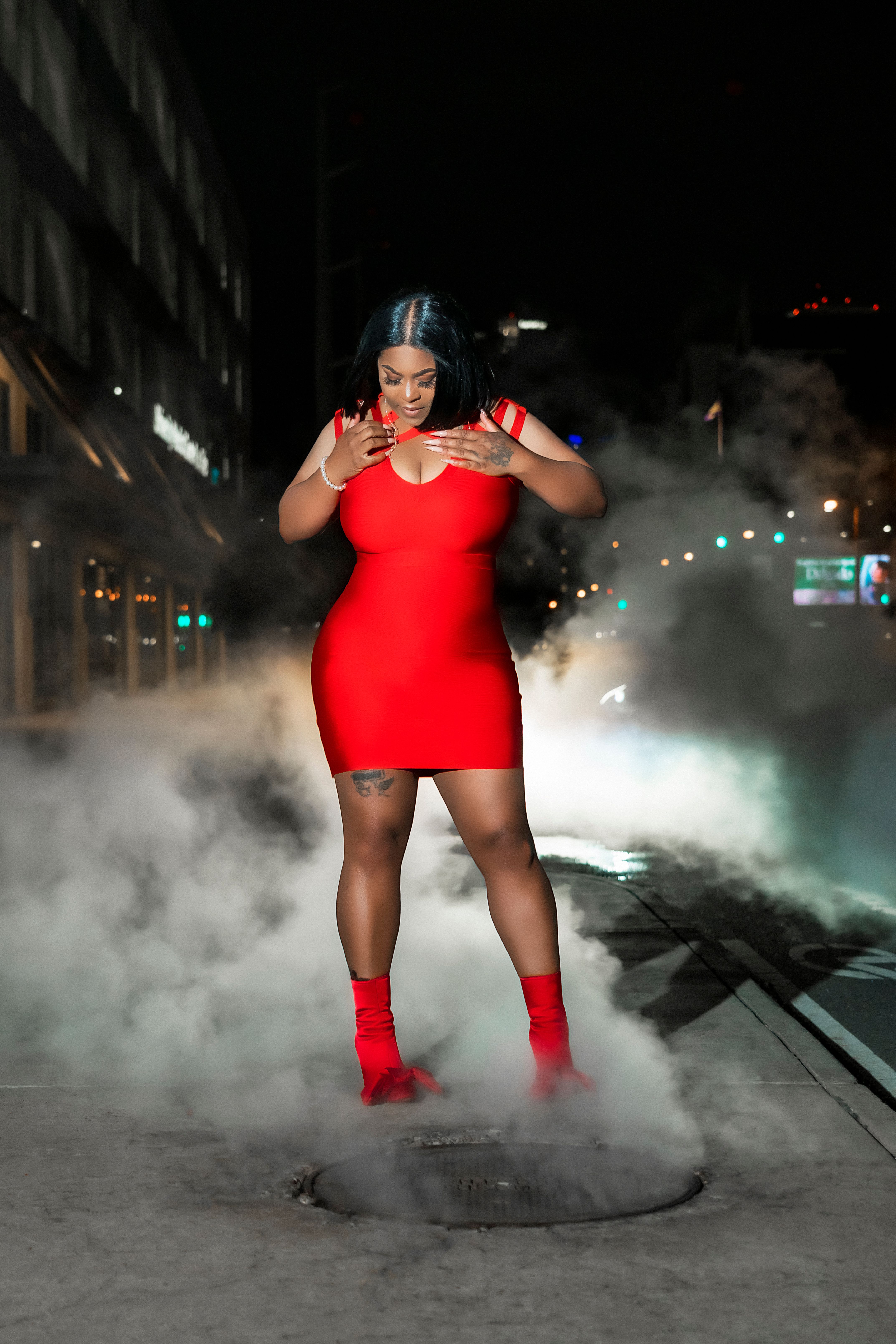 A striking portrait of a woman in a red dress amidst city steam on a New Orleans street at night.