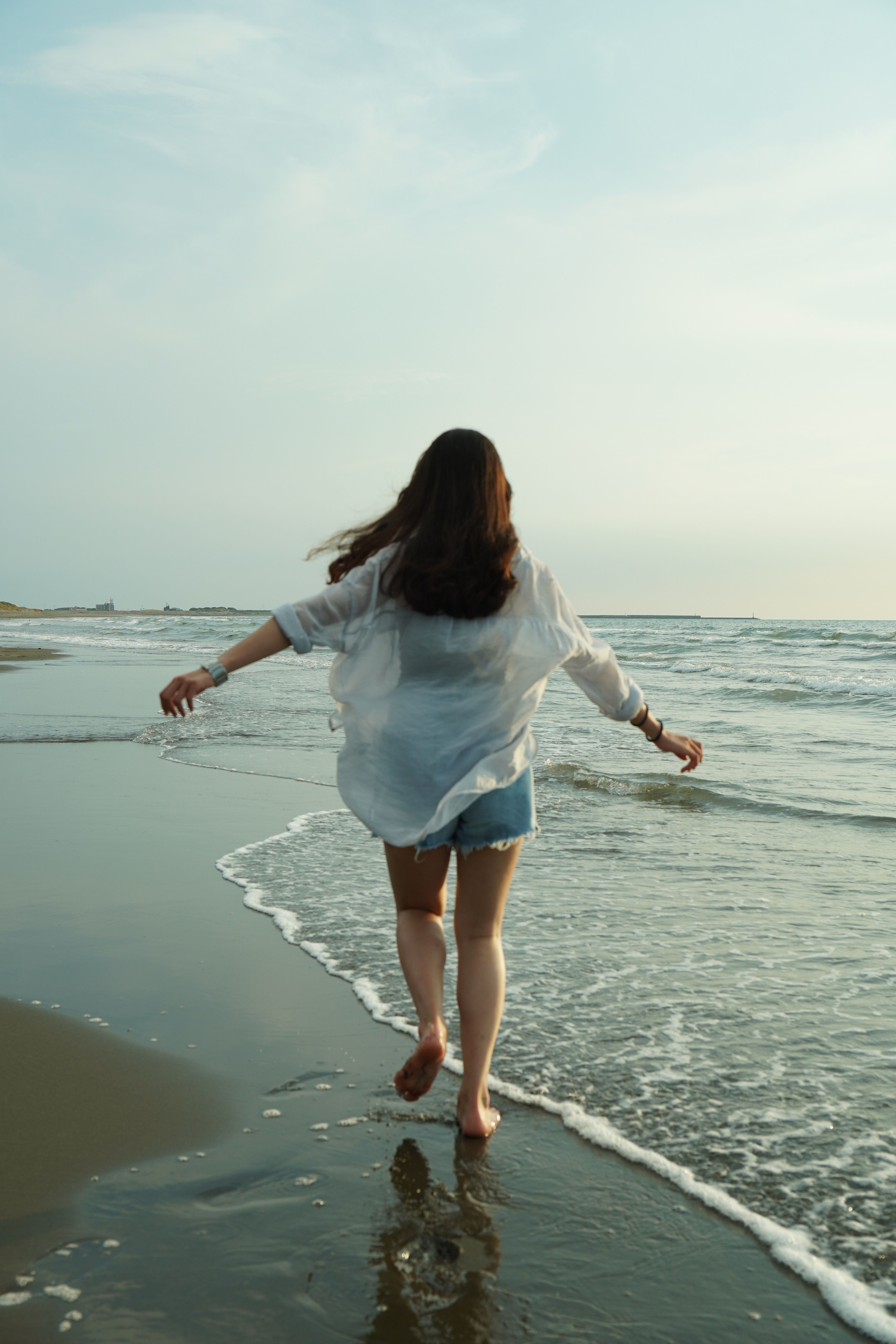 A woman walking along the beach, enjoying a tranquil moment by the sea at dusk.