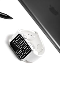 A sleek white smartwatch with a digital display on a minimalist desk setup.