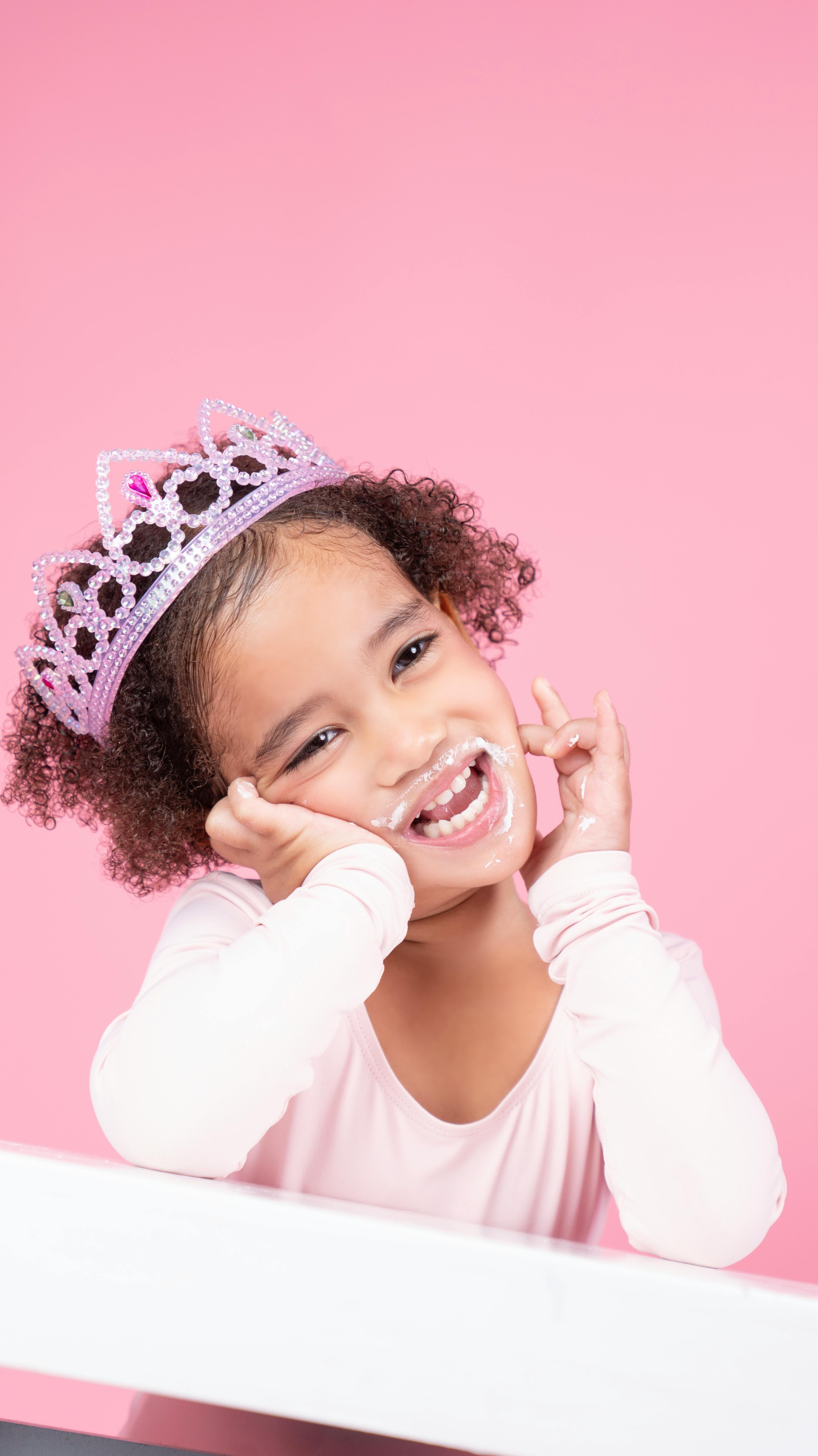 Smiling child with vitiligo wearing a crown against a pink background. Charming portrait.