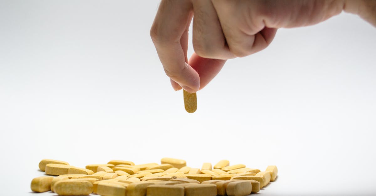 Primer plano de una mano que toma una pastilla amarilla de una pila de tabletas sobre una superficie blanca. Primer plano de una mano que toma una pastilla amarilla de una pila de tabletas sobre una superficie blanca.