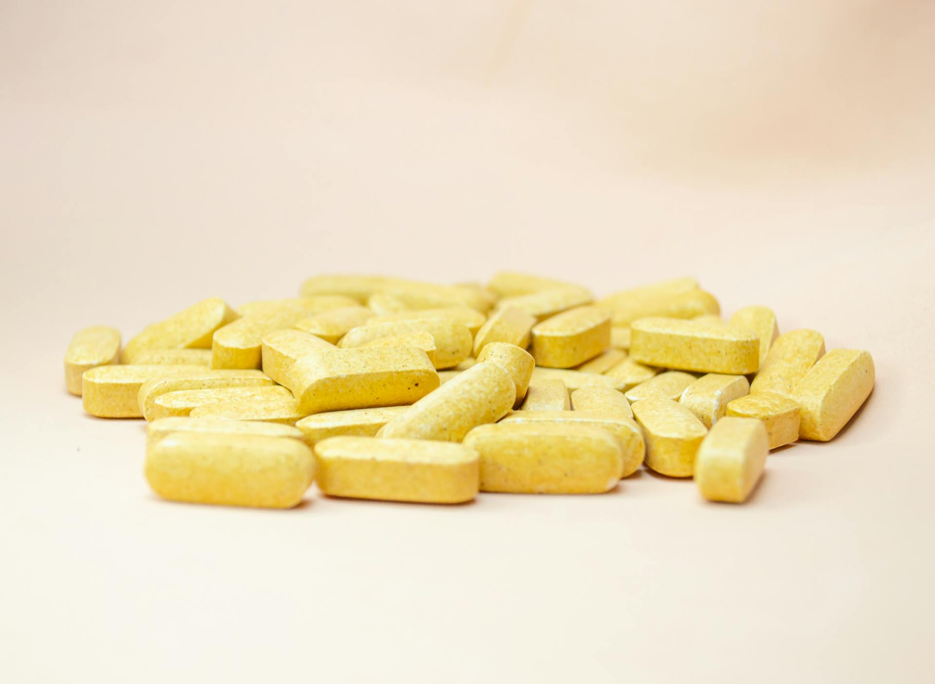 Close-up of scattered yellow vitamin tablets on a light neutral background.