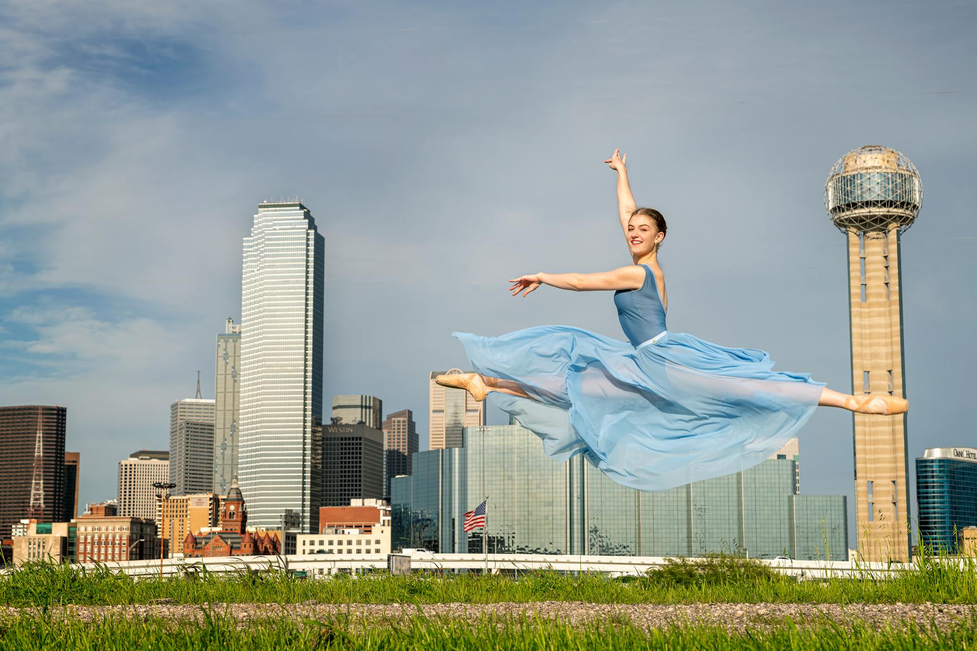 Graceful ballet dancer performing a leap with Dallas skyline in the background.