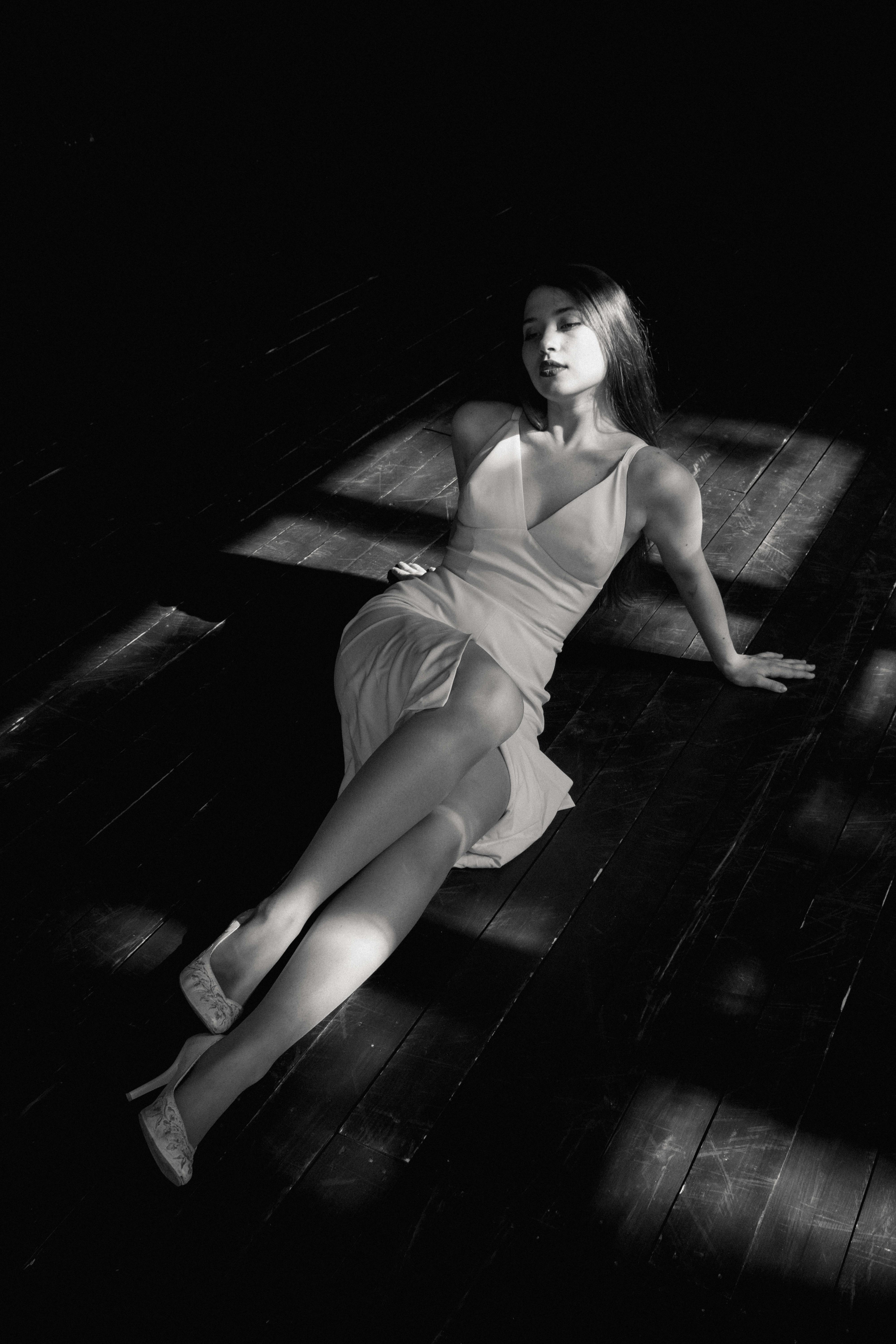 A woman in a white dress poses gracefully on a dark floor with dramatic lighting.