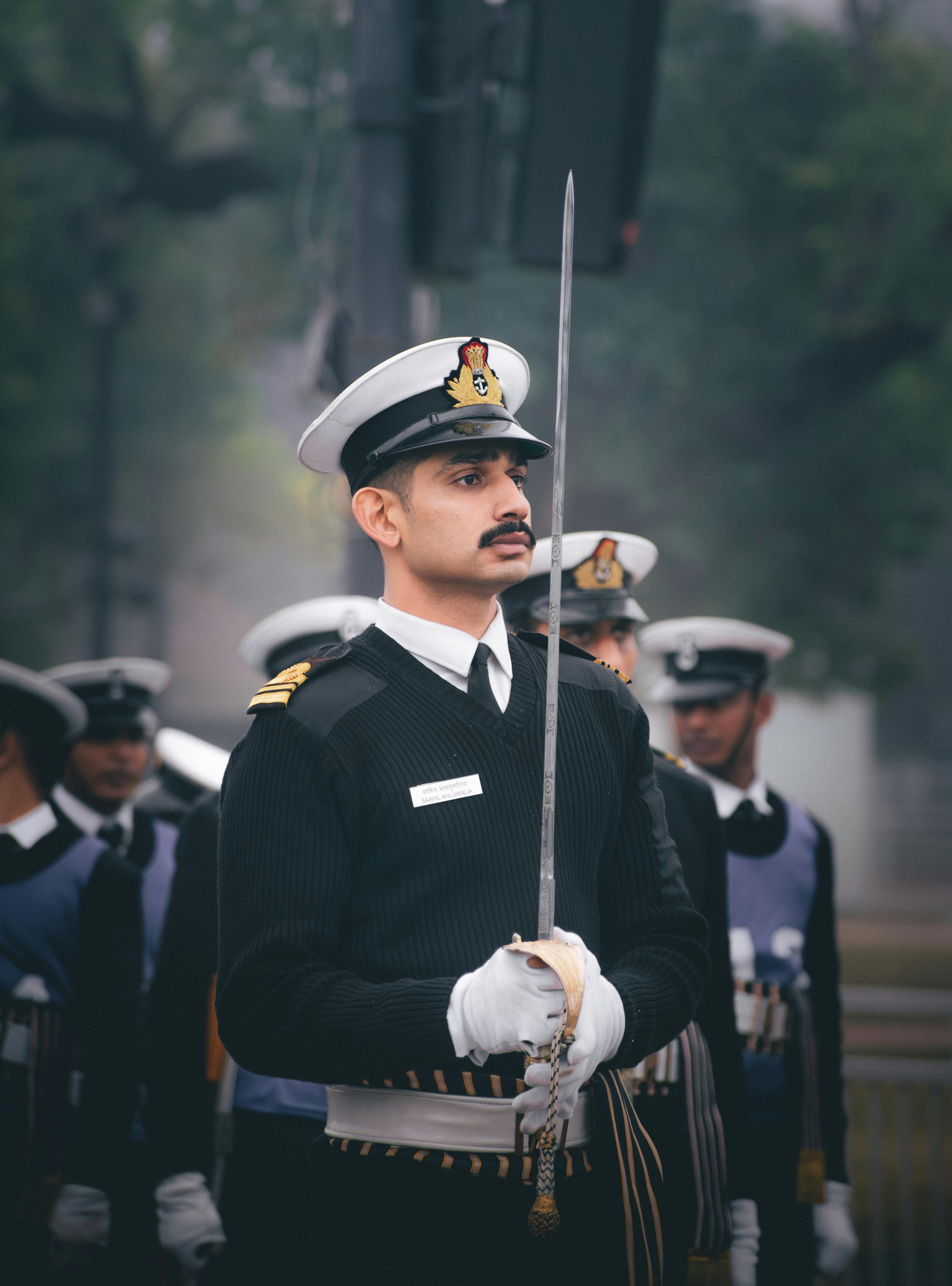 A uniformed navy officer holding a sword during a ceremonial parade outdoors.