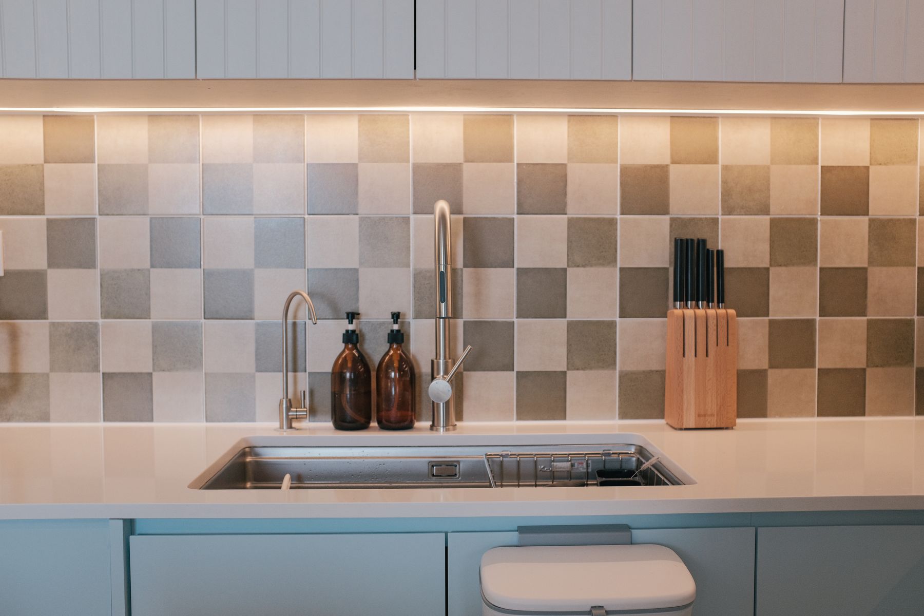Kitchen sink and pale tiled backsplash with restrained countertop tones and nearby kitchen utensils