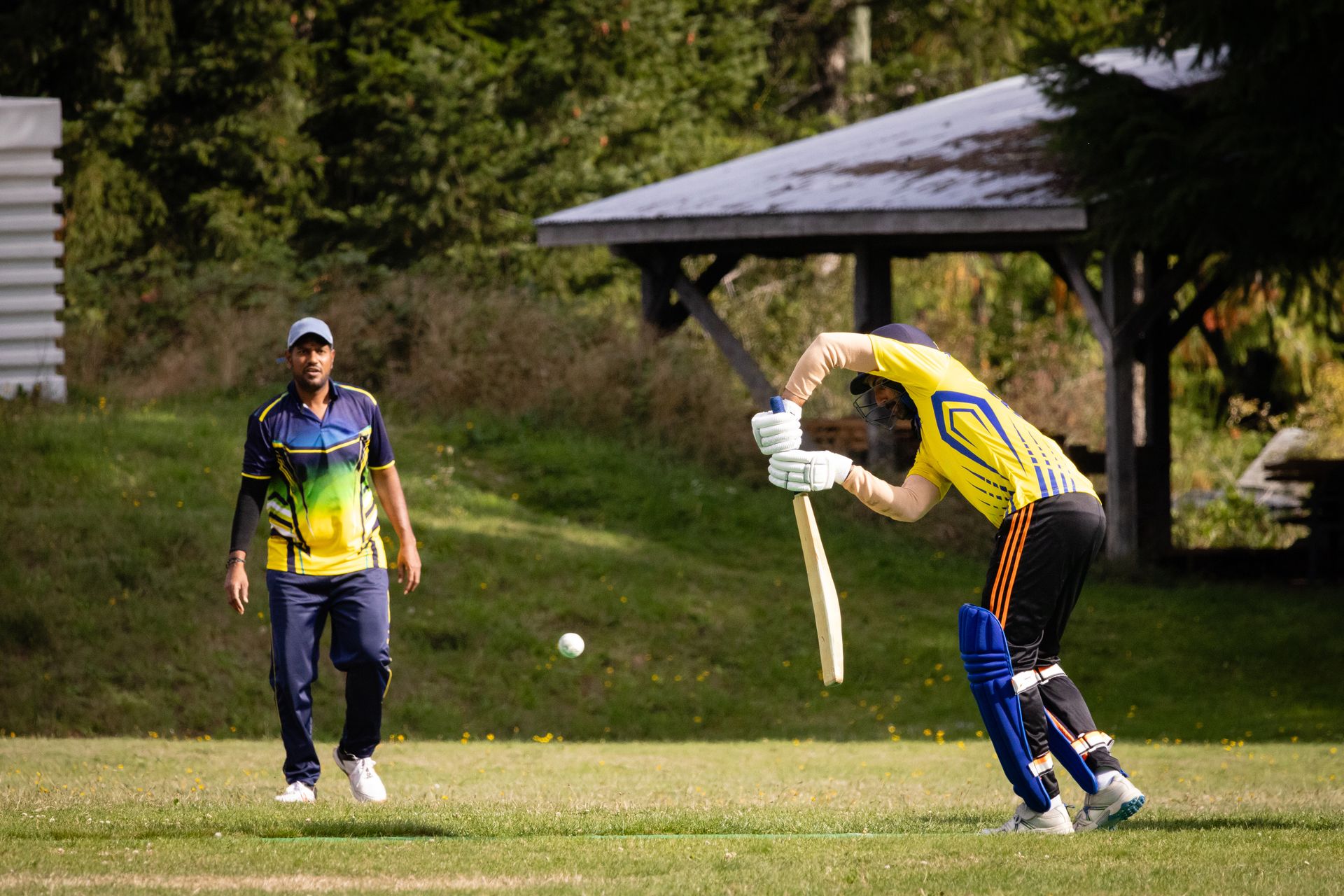 Two cricketers engaged in an outdoor match, focusing on batting and fielding tactics.