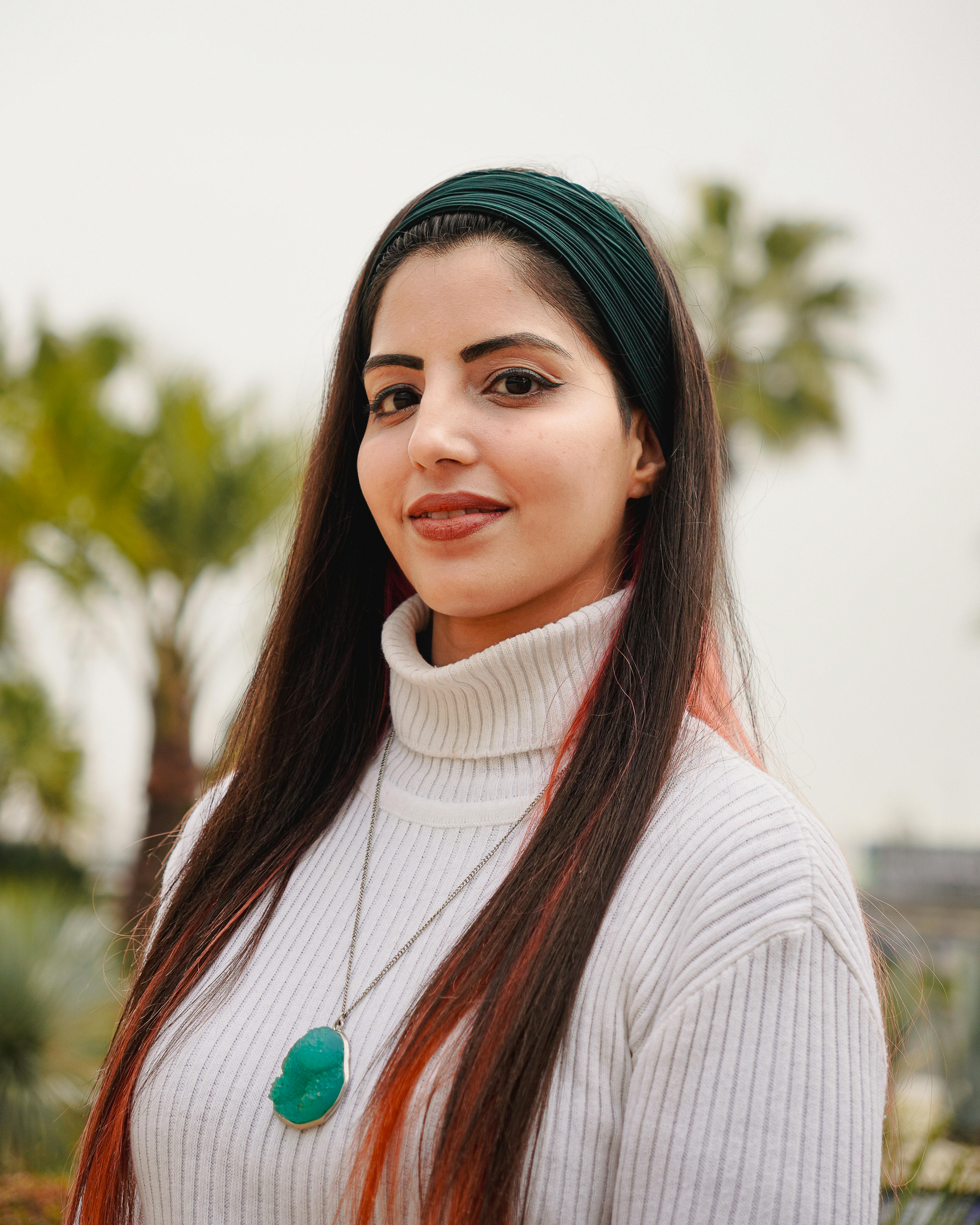Stylish young woman poses confidently outdoors against palm trees in Istanbul.