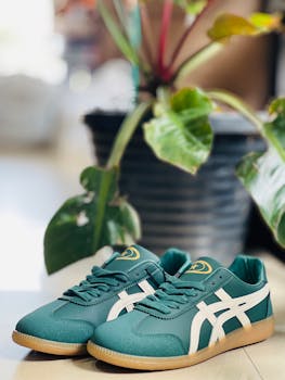 Fashionable green sneakers with white stripes beside a potted plant indoors.