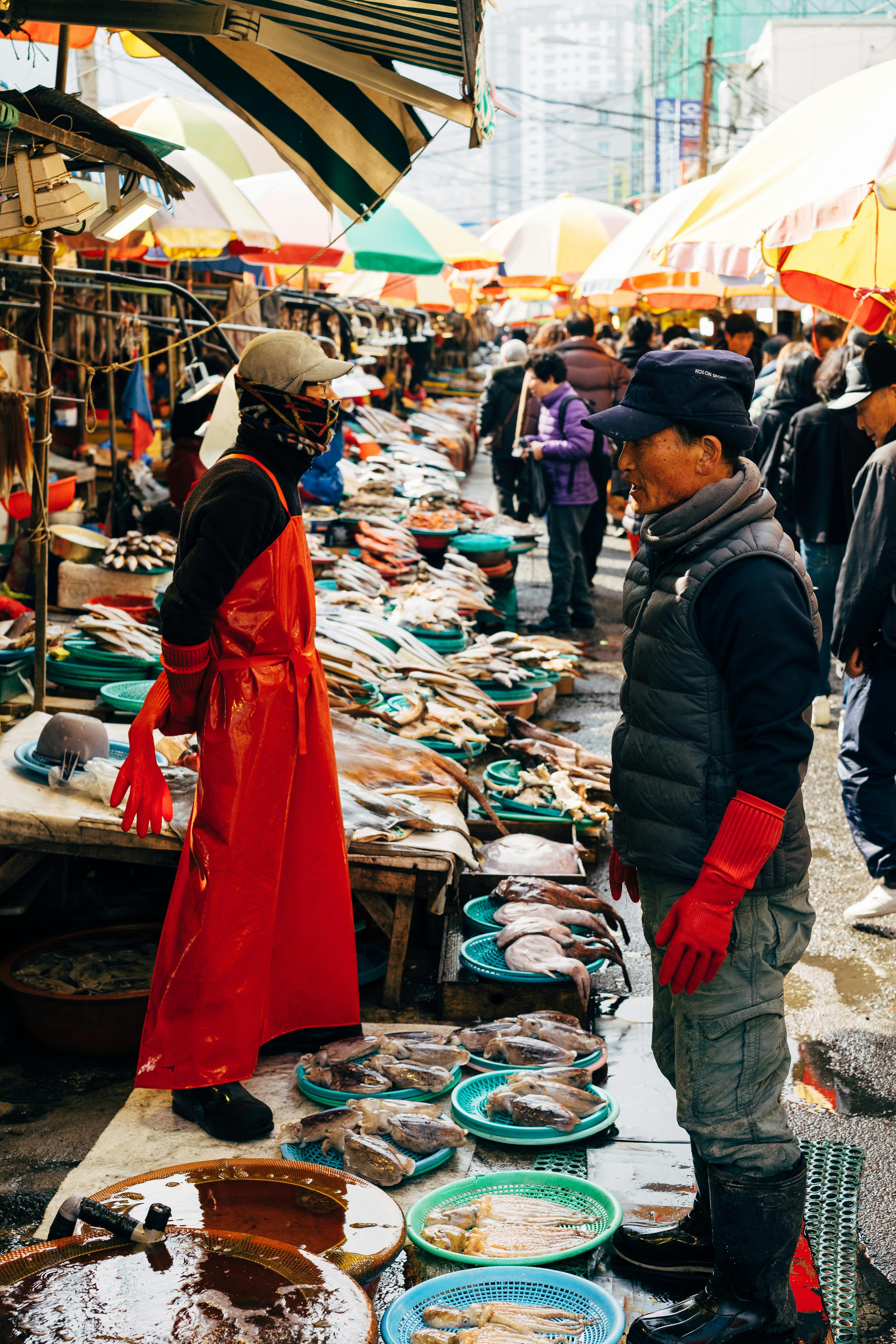 a crowd of people in the fish market lined with colorful umbrellas