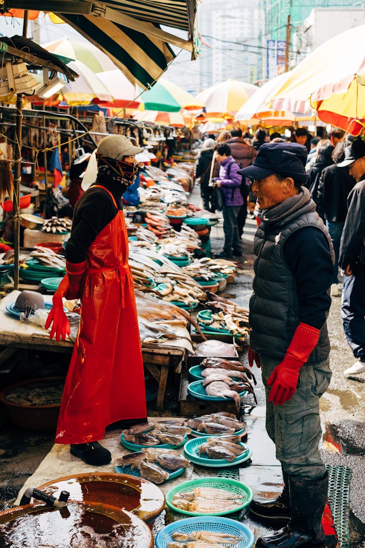 A Crowd Of People In The Fish Market Lined With Colorful Umbrellas