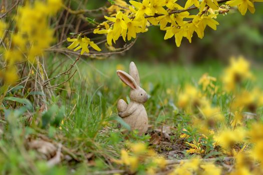 A charming wooden bunny nestled in grass, surrounded by bright yellow spring flowers.
