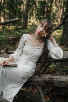 A young woman in a white dress rests on a fallen tree in a lush forest setting.