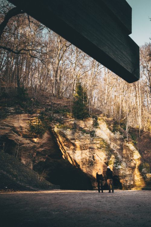 Free Couple walking in a forest area near a cave with beautiful sunlit trees. Stock Photo