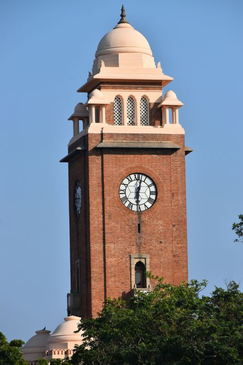 Free A historic red brick clock tower with ornate design set against a clear blue sky. Stock Photo