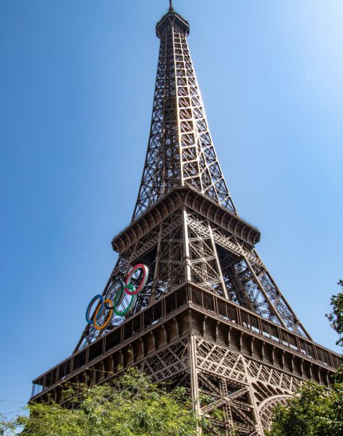 Free Eiffel Tower adorned with Olympic rings under clear blue sky, Paris landmark. Stock Photo