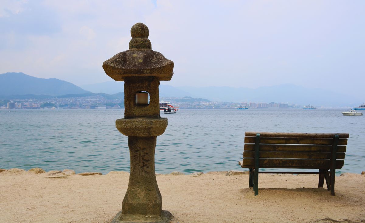 Stone lantern and bench beside the calm sea in Hiroshima, Japan, evoking the quiet seaside temples and viewpoints of Tomonoura