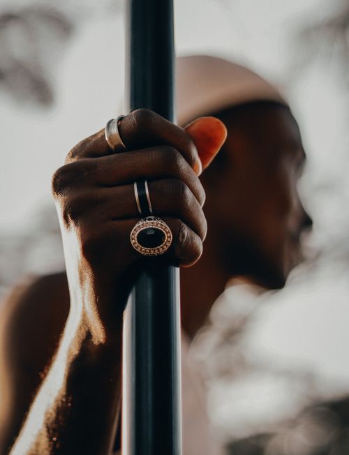Free Artistic shot of a hand adorned with silver rings holding a metal pole. Blurred person in background. Stock Photo