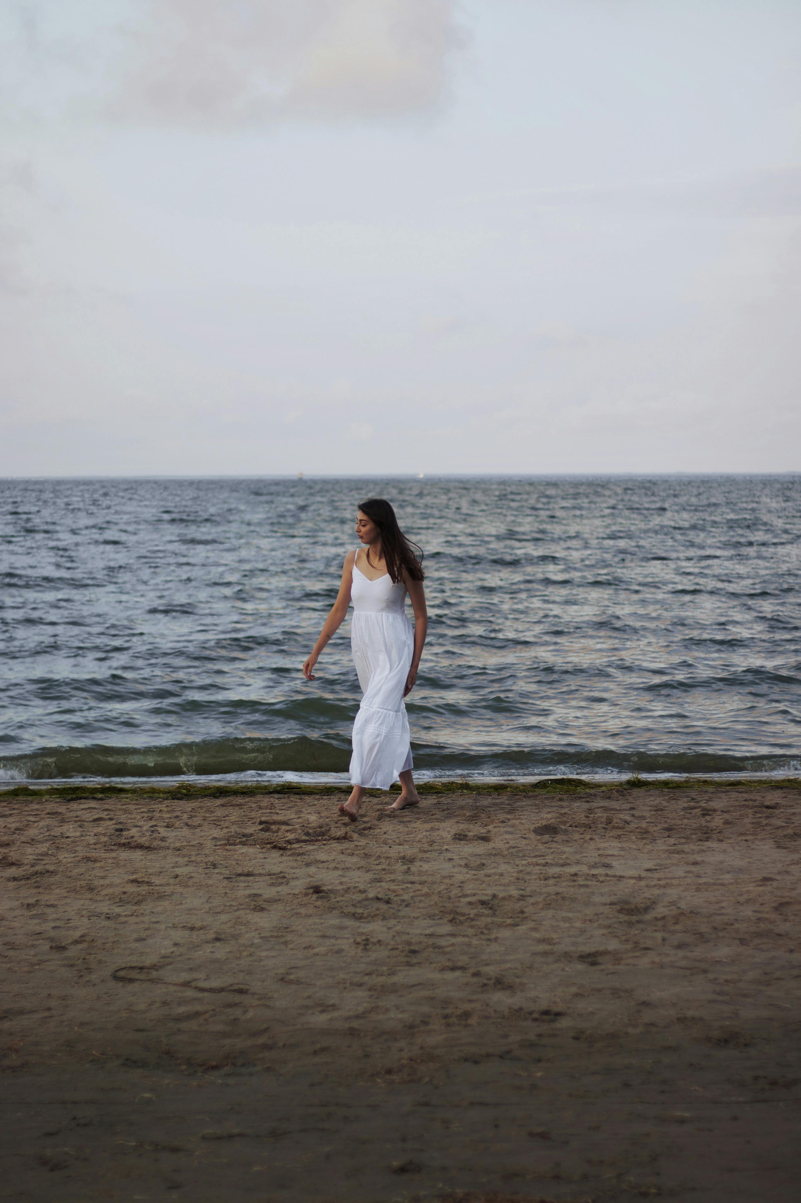 Elegant woman strolling on a serene beach, enjoying a warm summer day.