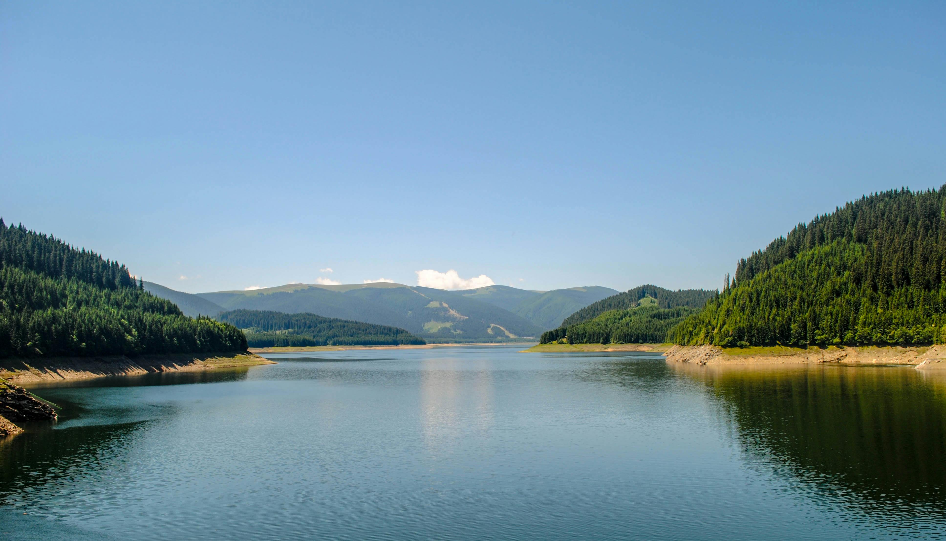 Serene mountain lake surrounded by lush forests under a clear blue sky.