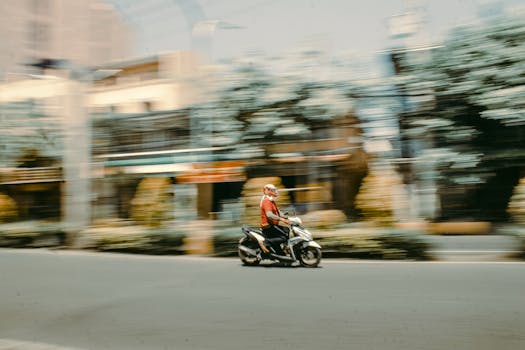 Blurred motion shot of a motorcyclist speeding through an urban street during the day, showcasing city life and transportation.