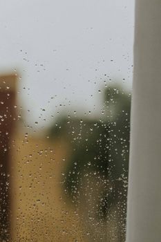 Rain droplets on a window with a blurred outdoor view, evoking a serene and contemplative mood.