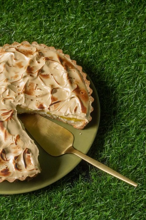 Free Sliced lemon meringue pie with golden crust on grass, served with gold cake server. Stock Photo