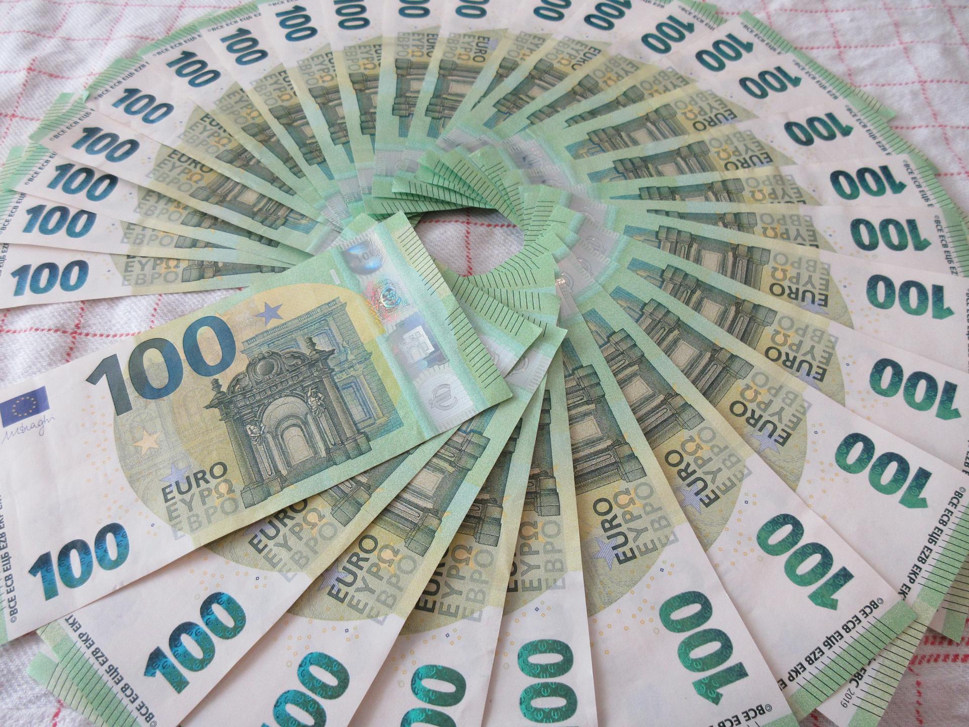 Close-up of a fan of 100 euro banknotes arranged in an artistic circle pattern on a textile surface.