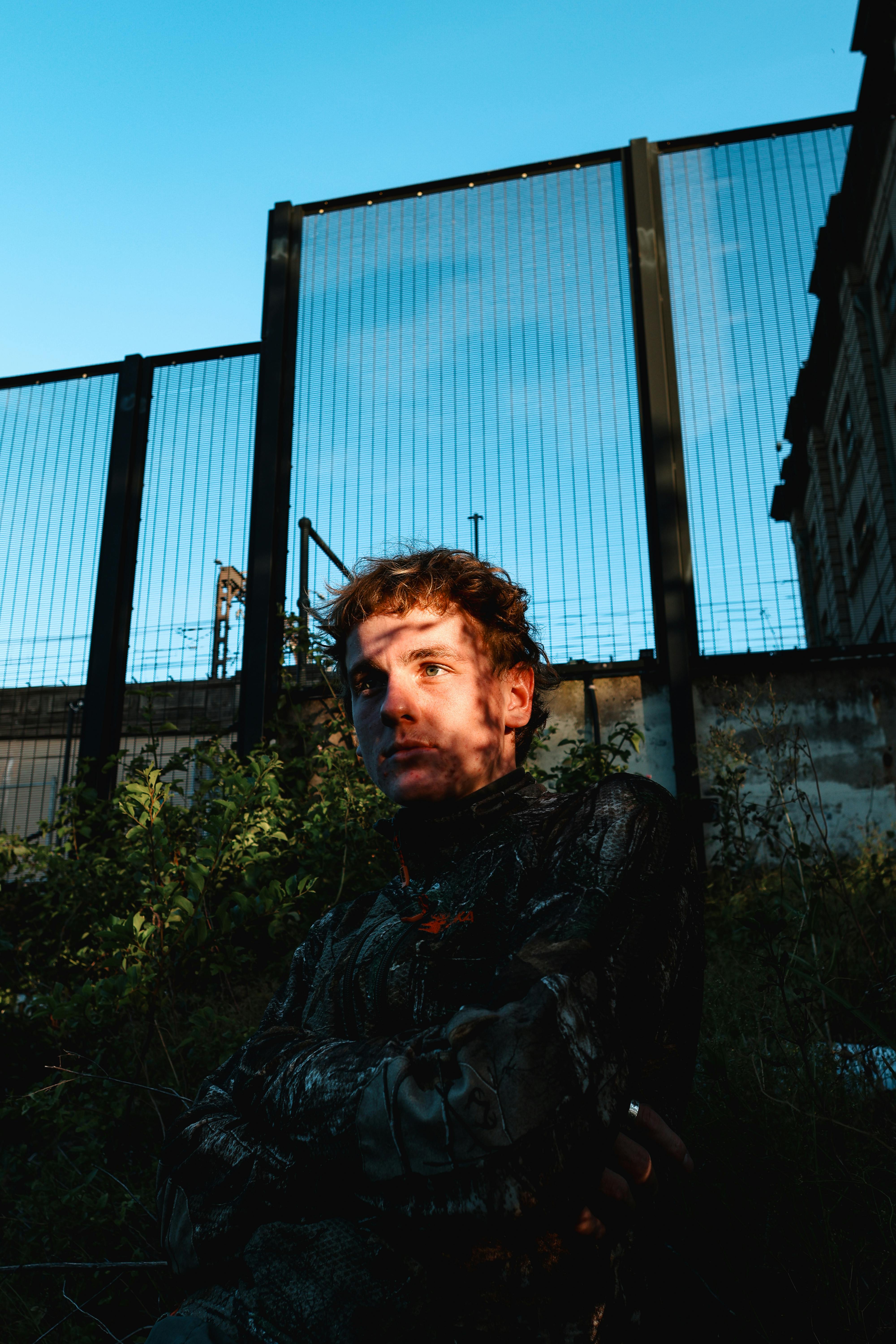 bezplatná Dramatický portrét člověka na pozadí průmyslového plotu. Základová fotografie