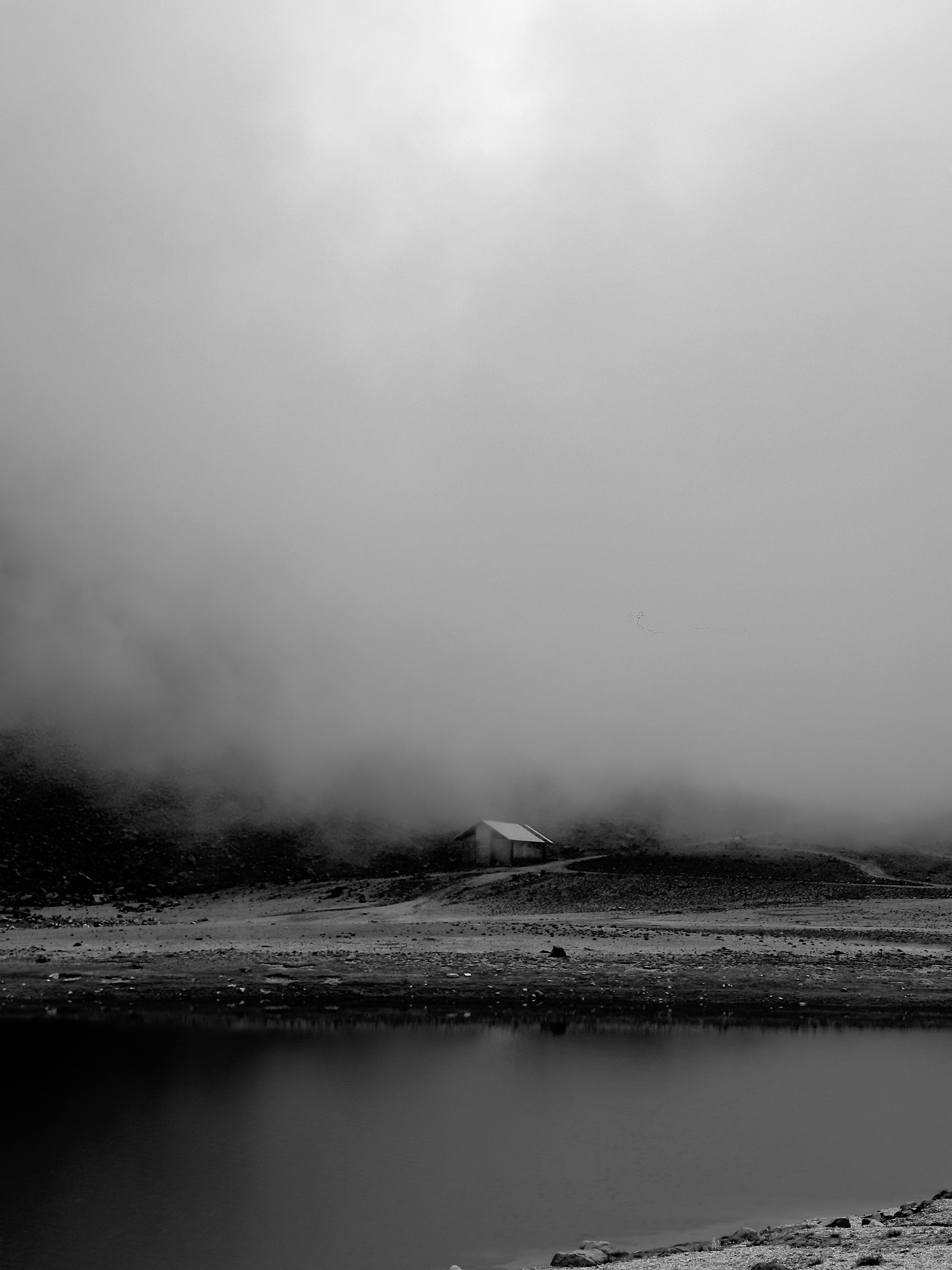 A serene, moody landscape with a solitary cabin amidst misty mountains and calm lake.