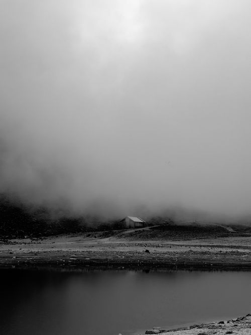 Free A serene, moody landscape with a solitary cabin amidst misty mountains and calm lake. Stock Photo