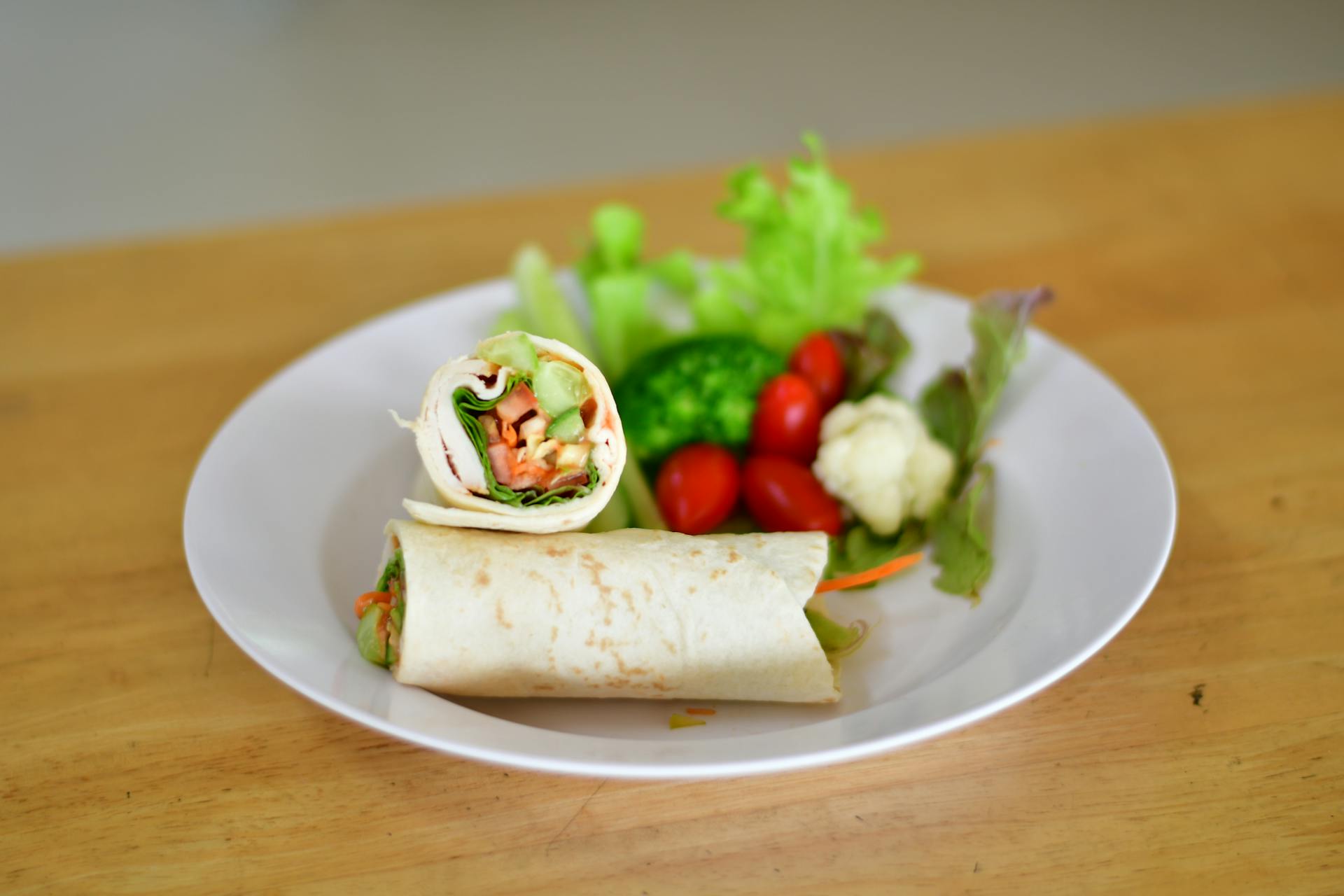 Delicious vegetable wrap with fresh greens and cherry tomatoes on a white plate.