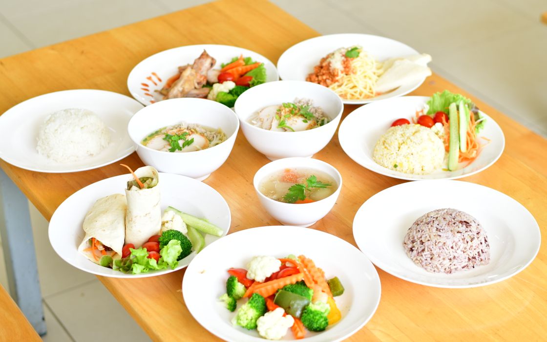 A variety of healthy dishes including rice, soup, and vegetables served on a wooden table.