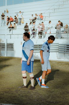 Players in a soccer match on a sunny day with fans watching from the bleachers.