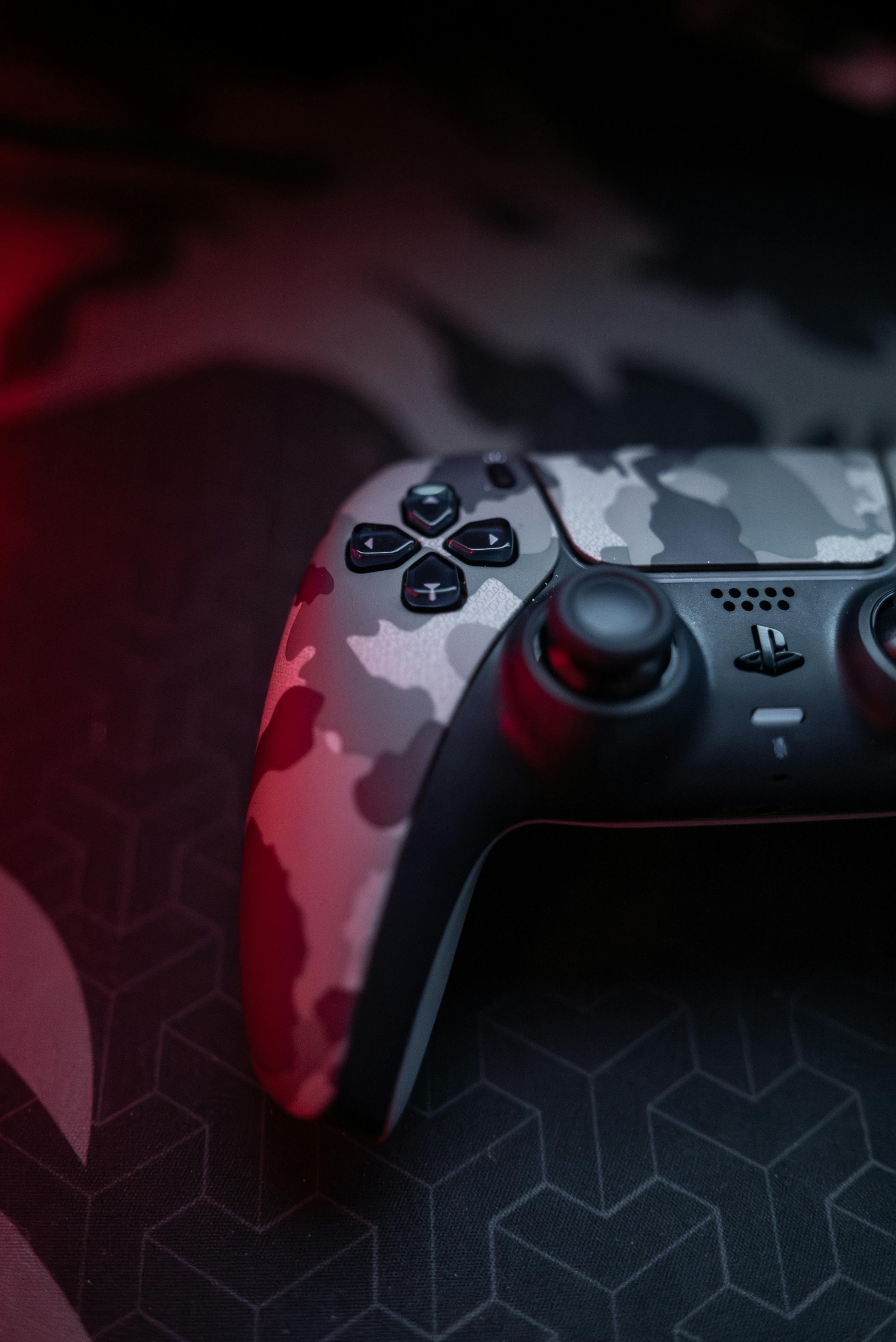 Close-up of a camouflage gaming controller on a dark patterned surface with red lighting.