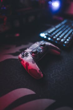A camouflaged gaming controller rests on a desk next to an illuminated keyboard, creating a modern gaming vibe.