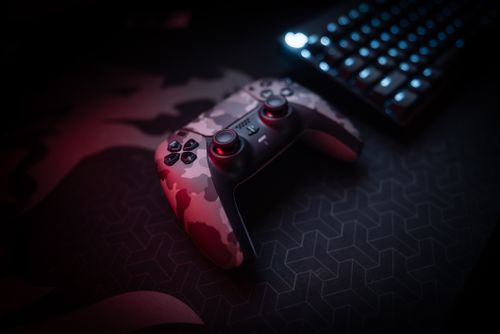 Free Close-up of a camouflage gaming controller and keyboard with red lighting ambiance. Stock Photo