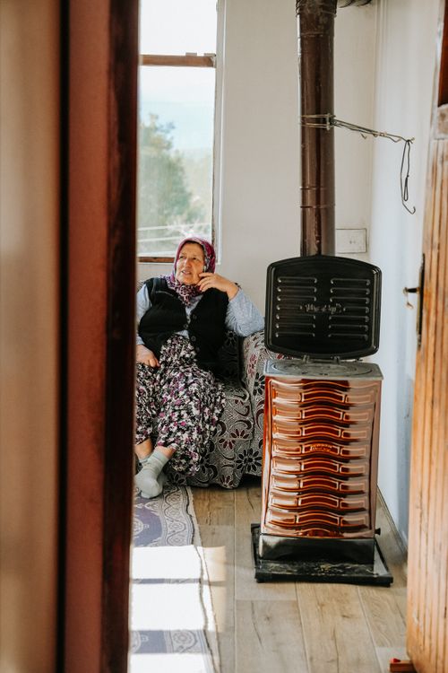 Free Senior woman sitting by a vintage stove indoors, enjoying a cozy atmosphere. Stock Photo