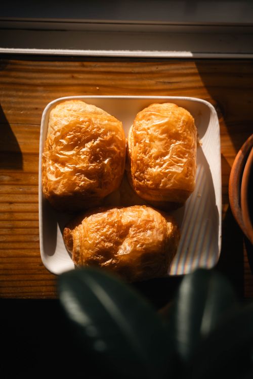 Free Three golden pastries on a plate with warm sunlight in a cozy indoor setting. Stock Photo
