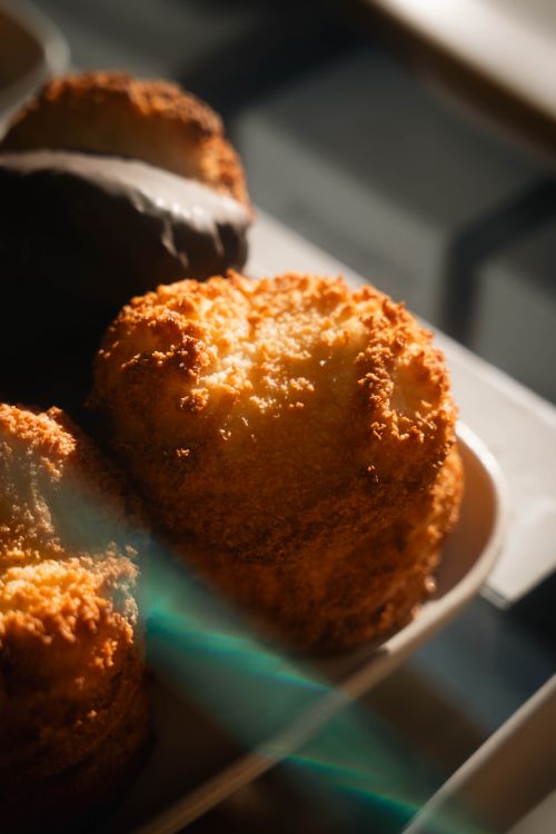 Free Delicious golden coconut pastries stacked in warm sunlit display, tempting and fresh. Stock Photo