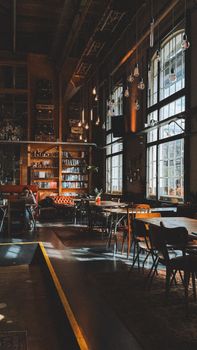 Warm and inviting industrial-style café interior with large windows in Tilburg, Netherlands.